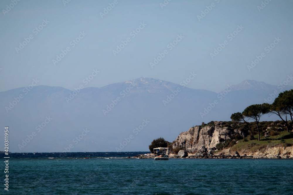Bay on the Aegean coast of Turkey with a view of the island of Chios in the background, trees and a boat
