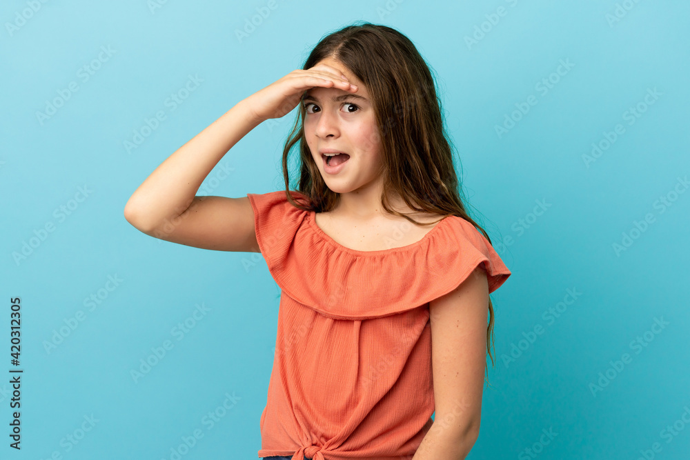 Little caucasian girl isolated on blue background doing surprise gesture while looking front