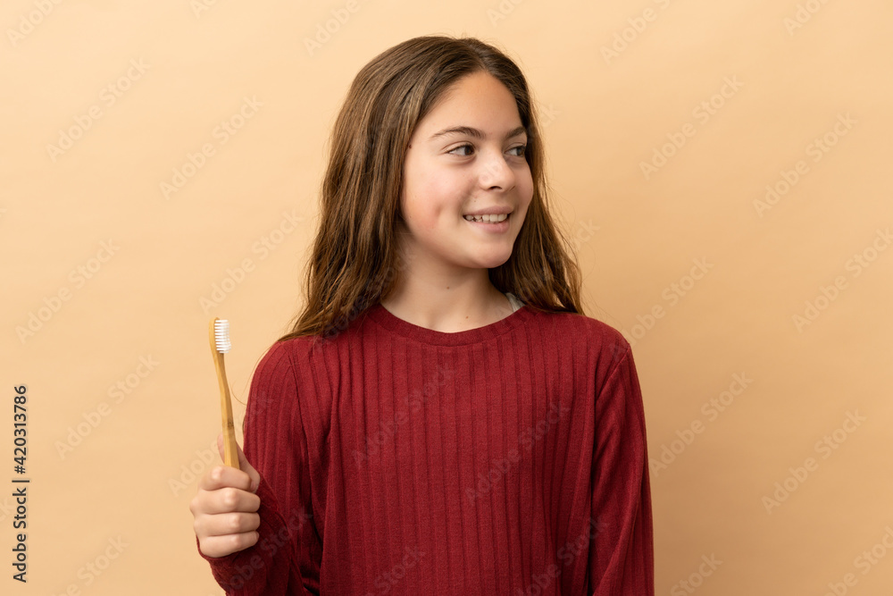 Little caucasian girl brushing her teeth isolated on beige background looking to the side and smiling Little caucasian girl brushing her teeth isolated on beige background looking to the side and smiling