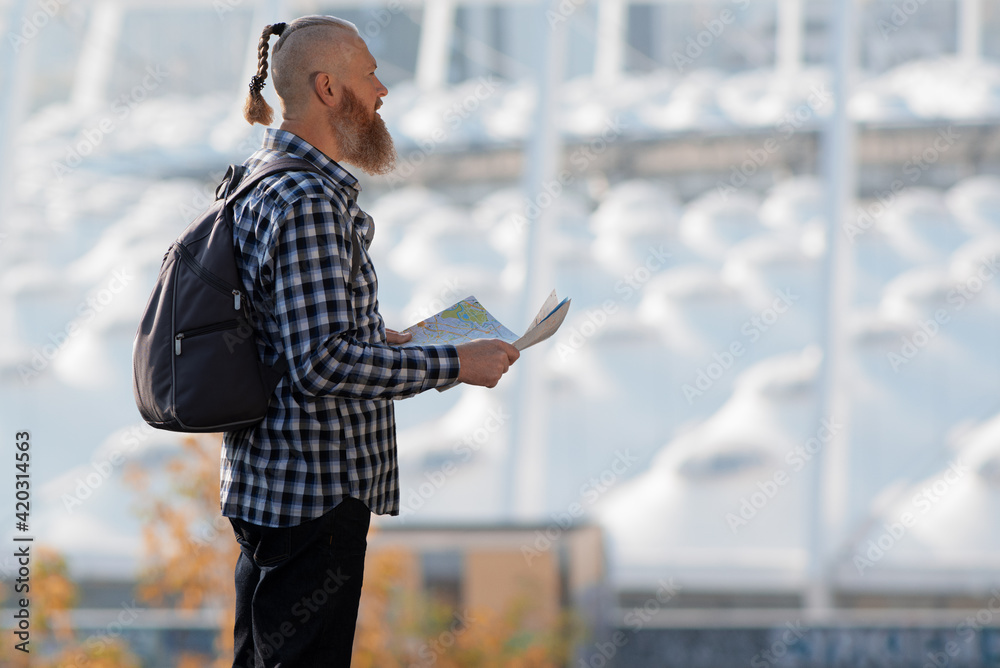 Man tourist holding map in hands planning route in big city. Side view. Copy space. Travel concept.