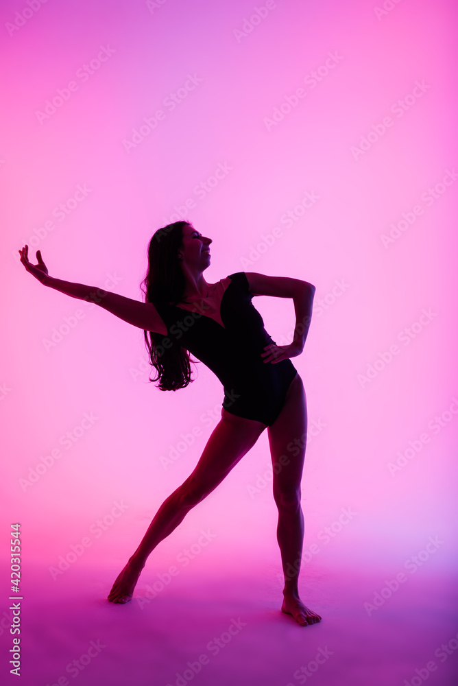 Professional ballerina dancing ballet in spotlights smoke. Beautiful young female wearing black bodysuit on floodlights background.