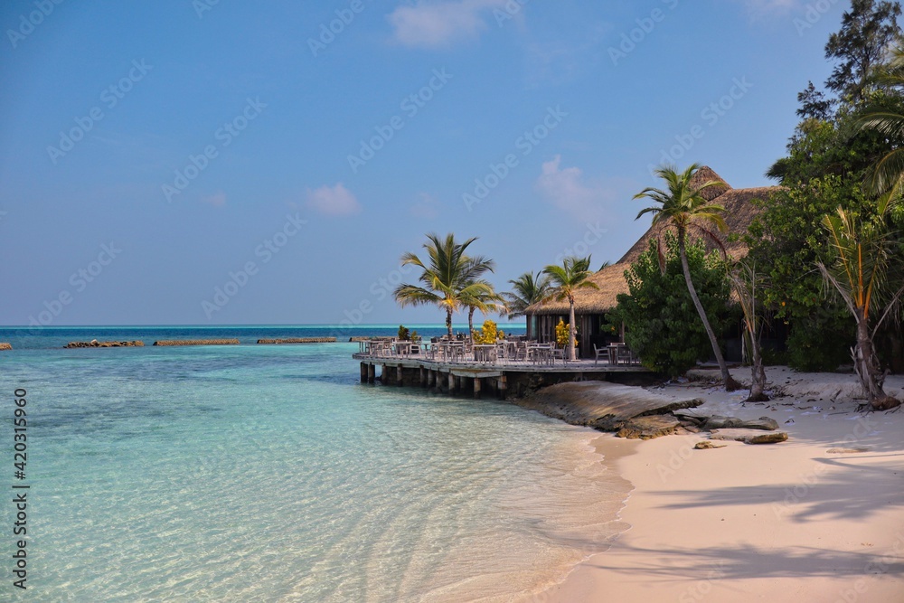Maldives Resort with Sandy Beach, Turquoise Sea and Thatched Restaurant. Sunny Day in Paradise. Maldivian Komandoo Island Resort.