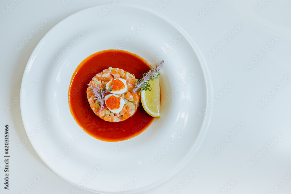 Top view of salmon tartare with tomato gazpacho and celery on white plate.