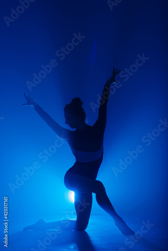Professional ballerina dancing ballet in spotlights smoke. Beautiful young female wearing black bodysuit on floodlights background.