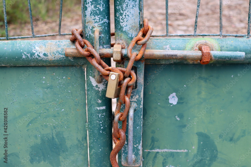 Metal gate locked by a padlock and rusty chain. Rusty iron chain. Metal gate locked by a padlock and rusty chain. Rusty iron chain.