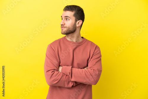 Handsome blonde man over isolated yellow background keeping the arms crossed