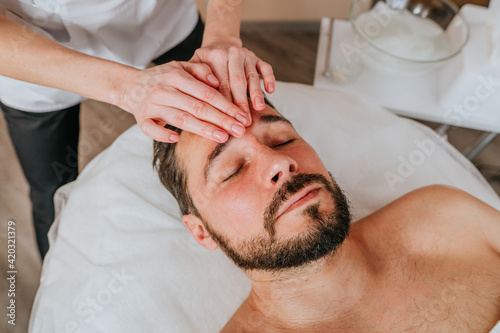 Esthetician or facialist gives a relaxing facial massage to a man