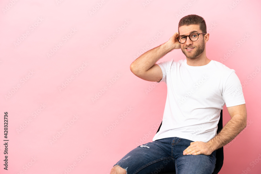 Fototapeta premium Young man sitting on a chair over isolated pink background having doubts