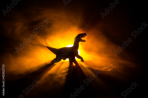 Fototapeta Naklejka Na Ścianę i Meble -  Silhouette of giant Dinosaur in dark foggy night. Creative decoration with little miniature. Burning misty background.