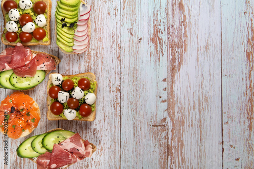 An assortment of sandwiches with fish, cheese, meat and vegetables lay on the wooden table photo