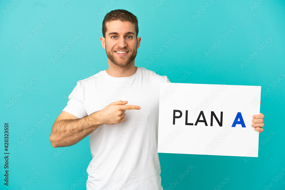 Handsome blonde man over isolated blue background holding a placard with the message PLAN A and pointing it Handsome blonde man over isolated blue background holding a placard with the message PLAN A and pointing it