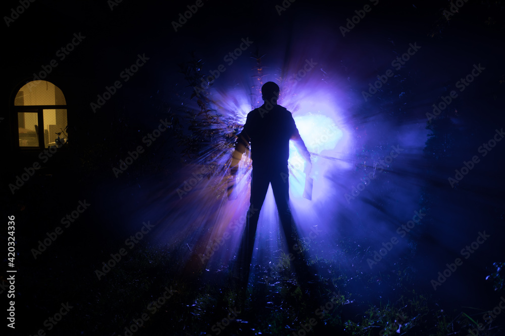 strange light in a dark forest at night. Silhouette of person standing in the dark forest with light. Horror halloween concept. strange silhouette in a dark spooky forest at night strange light in a dark forest at night. Silhouette of person standing in the dark forest with light. Horror halloween concept. strange silhouette in a dark spooky forest at night