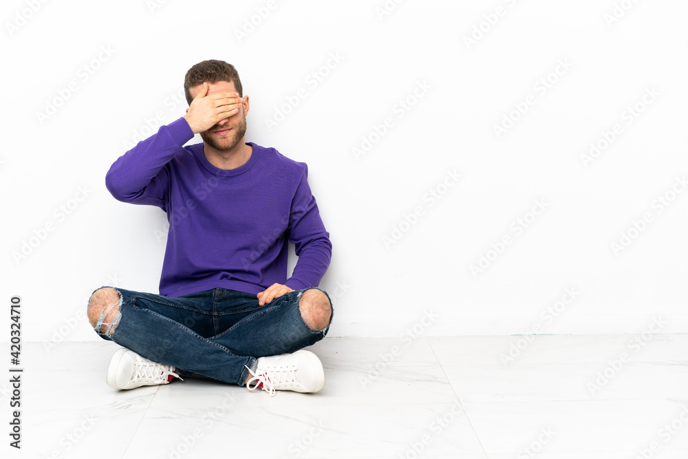 Young man sitting on the floor covering eyes by hands. Do not want to see something