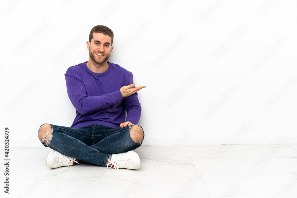 Young man sitting on the floor presenting an idea while looking smiling towards Young man sitting on the floor presenting an idea while looking smiling towards