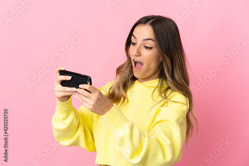 Young Romanian woman isolated on pink background playing with the mobile phone