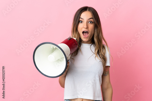 Young Romanian woman isolated on pink background holding a megaphone and with surprise expression