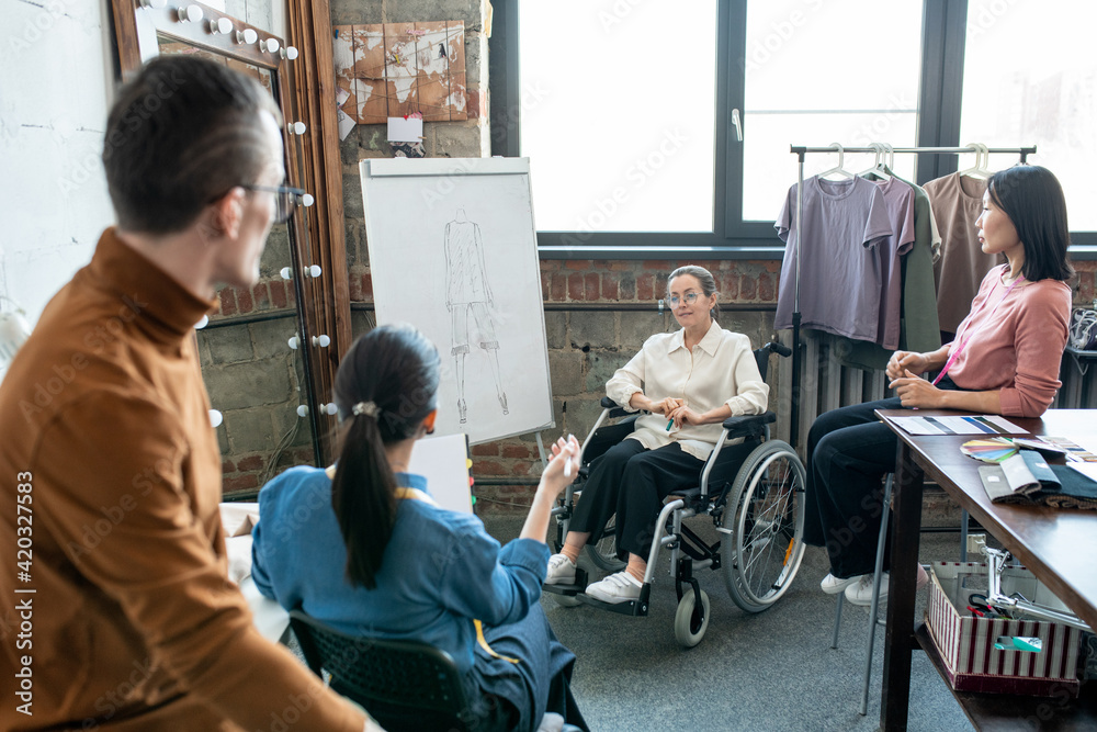 Young disable female designer by whiteboard and other colleagues discussing sketch of new model Young disable female designer by whiteboard and other colleagues discussing sketch of new model