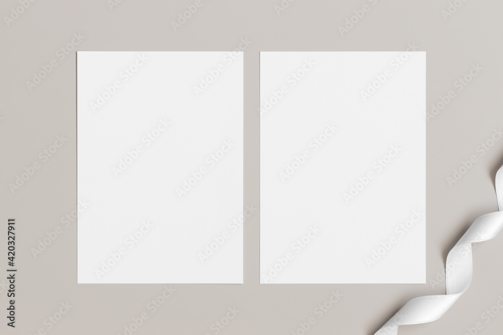 Two white invitation cards mockup with a satin tape decoration on the beige table. 5x7 ratio, similar to A6, A5. Two white invitation cards mockup with a satin tape decoration on the beige table. 5x7 ratio, similar to A6, A5.
