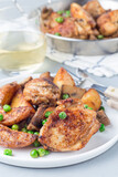 Chicken with potatoes, mushrooms and green peas, on a white plate and in metal pot, vertical