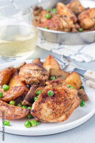 Chicken with potatoes, mushrooms and green peas, on a white plate and in metal pot, vertical