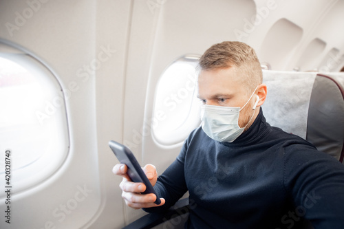 Male with safe mask passenger of airplane use mobile phone in chair. Concept travel covid