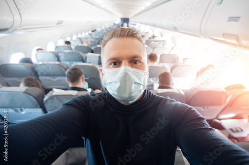 Portrait of tourist man in medical mask in airplane, concept travel trip in covid