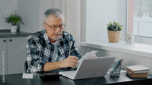 An unhappy elderly man gets upset while counting household expenses.