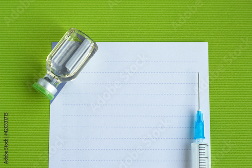Vaccination concept. Medicine ampoule and syrenge are near the note blank on the green background. Flat lay. Copy space for text. The portfolio has more vaccination pictures. photo