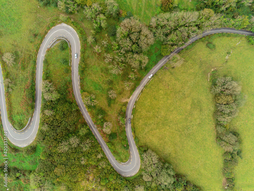 Winding narrow road on a hill in Burren, Ireland. Aerial drone view. Green fields and small trees around the pass.