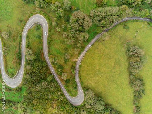Winding narrow road on a hill in Burren, Ireland. Aerial drone view. Green fields and small trees around the pass. © mark_gusev