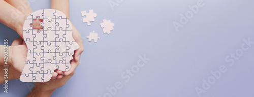 Adult and children hands holding brain with puzzle paper cutout, autism, memory loss, dementia, epilepsy and alzheimer awareness, world mental health day concept