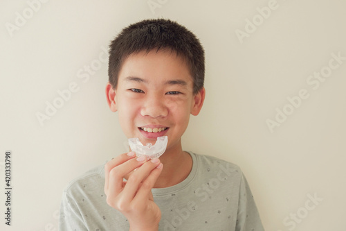 Smiling Asian preteen boy holding invisalign braces, mouthguard, teen orthodontic oral health care concept photo