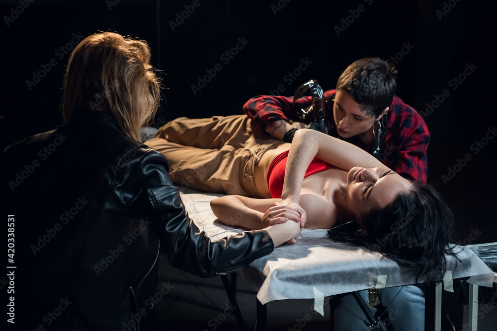 Obraz premium During the tattooing of a young pretty artist girl friend holds the client's hand as a sign of support.