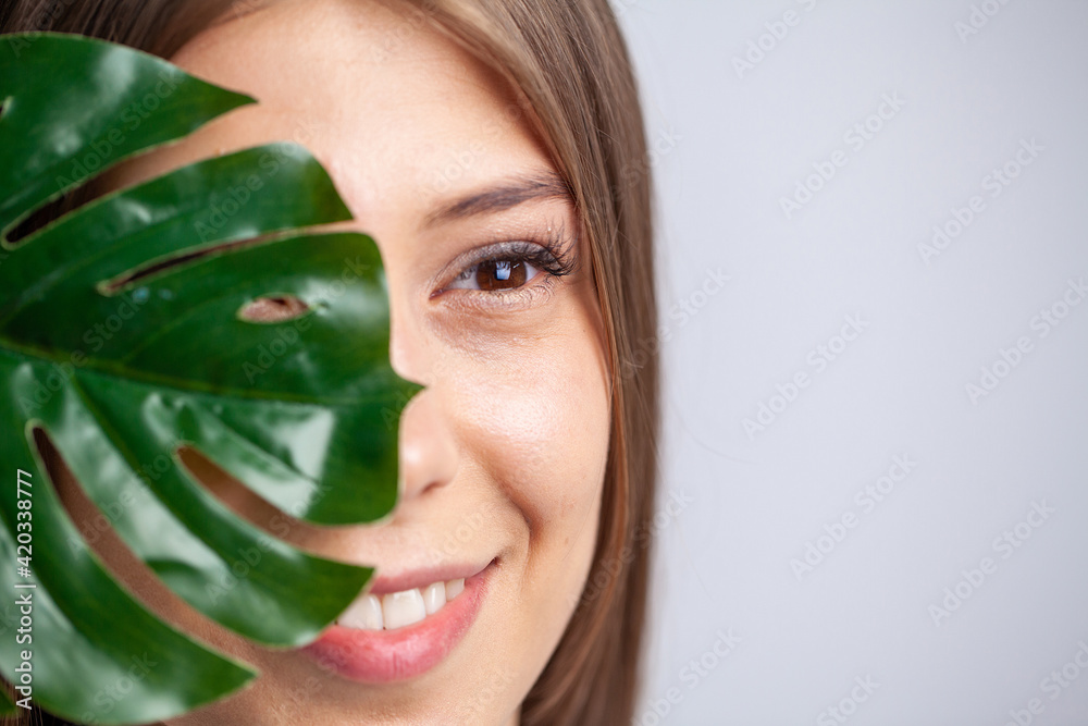 Cheerful woman with a smile holds a leaf of a flower near face Cheerful woman with a smile holds a leaf of a flower near face