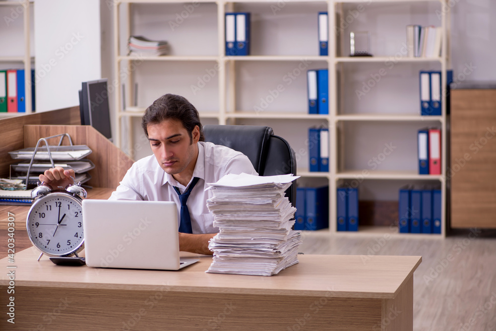 Young male employee in time management concept in the office Young male employee in time management concept in the office