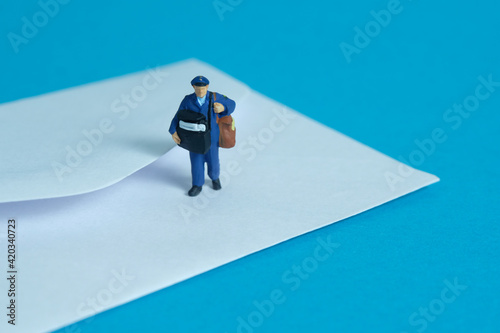 Miniature people toys conceptual photography. Mail postal courier delivery. Postman courier with envelope, isolated on blue background.