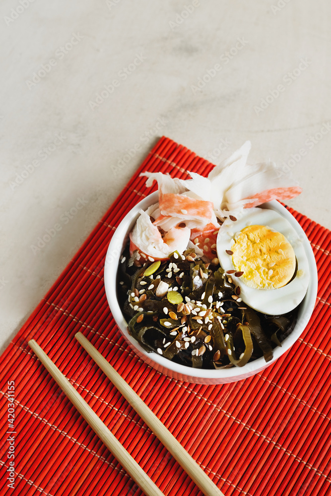 home cooking seaweed salad, crab, egg, sesame and pumpkin seeds on red Asian napkin and chopsticks. veganism in food. simple asian recipes at home. seaweed dishes.selective focus home cooking seaweed salad, crab, egg, sesame and pumpkin seeds on red Asian napkin and chopsticks. veganism in food. simple asian recipes at home. seaweed dishes.selective focus