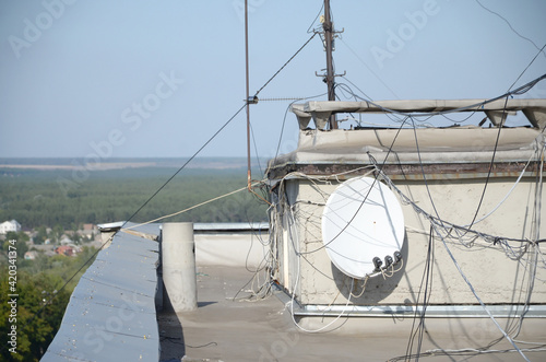 White satellite dish with three converters mounted on residental building rooftop concrete wall. Satellite television photo