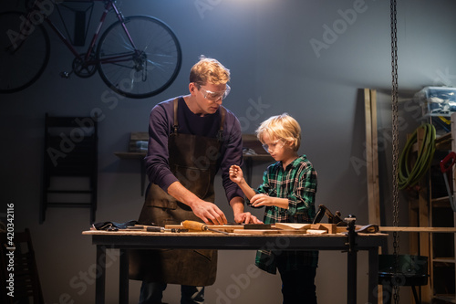Bild auf Leinwand a young father teaches the basics of carpentry to his son in the garage
