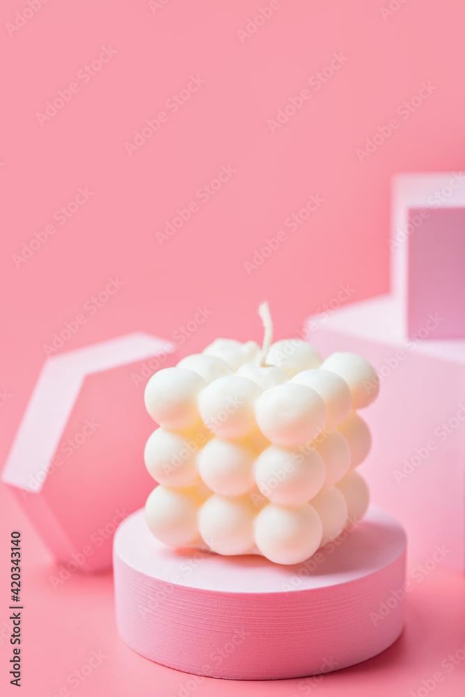 A trendy soy cube bubble candle on a pink podium at the pink background A trendy soy cube bubble candle on a pink podium at the pink background