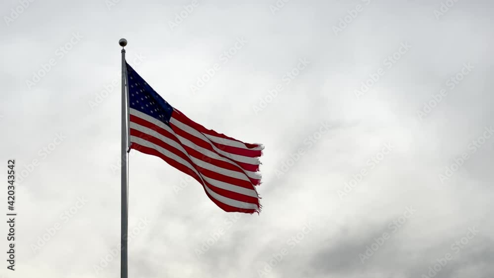 Damaged American flag waving in the wind against a cloudy sky. Ripped flag of the USA moving in the wind, patriotic background