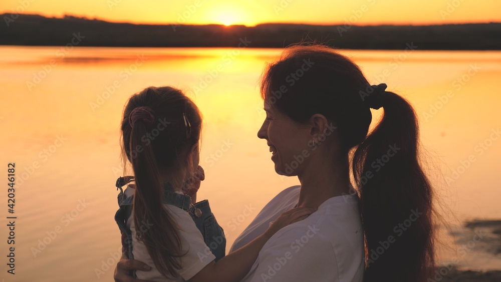 Happy mom holds a small child in her arms and plays with her noses laughing at sunset in the sky. Happy family life. Mom s day. Mother and daughter at dawn. Kid spend time with his parent. Maternal