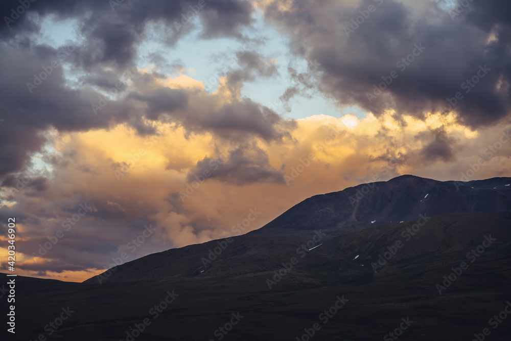 Beautiful mountain scenery with golden dawn light in cloudy sky. Scenic mountain landscape with illuminating color in sunset sky. Silhouettes of mountains on sunrise. Gold illuminating sunlight in sky