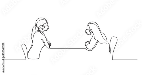 two young women wearing face masks sitting behind table talking