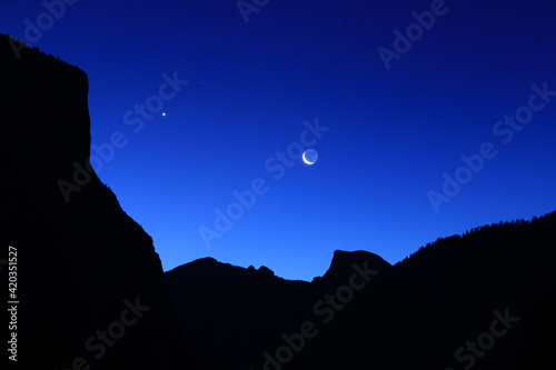 crescent moon over the silhouette of El Capitan and the Half Dome in Yosemite early dawn.