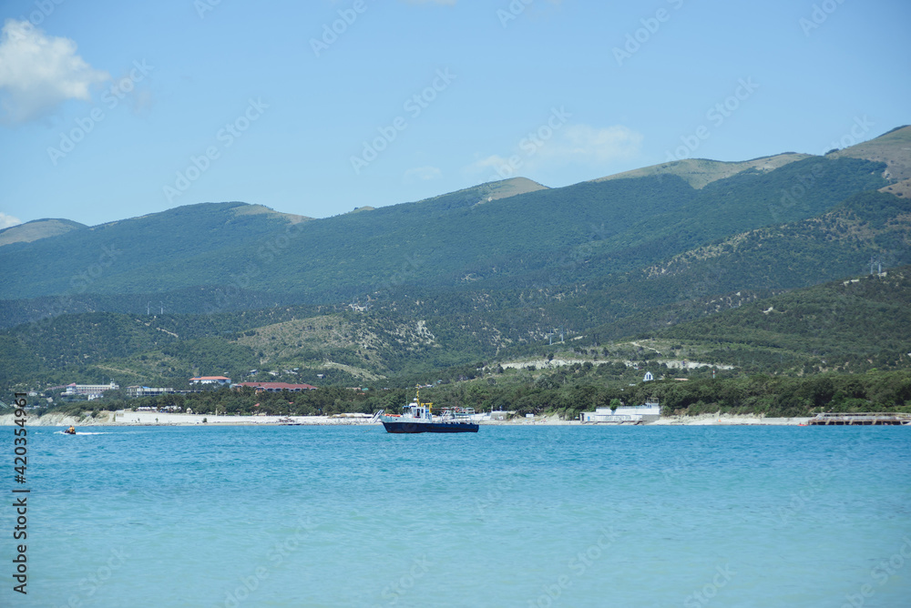 side view of small tourist boat without people in black sea bay on beach, mountains, and sky background, horizontal outdoors stock photo image