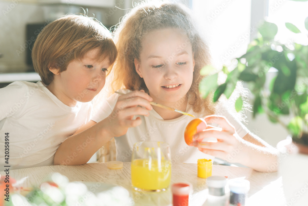 Two siblings brother and sister toddler boy tween girl painting easter eggs on kitchen at home on the spring sunny day Two siblings brother and sister toddler boy tween girl painting easter eggs on kitchen at home on the spring sunny day