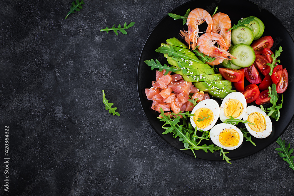 Ketogenic diet breakfast. Salt salmon salad with boiled shrimps, prawns, tomatoes, cucumbers, arugula, eggs and avocado. Keto, paleo lunch. Top view, overhead