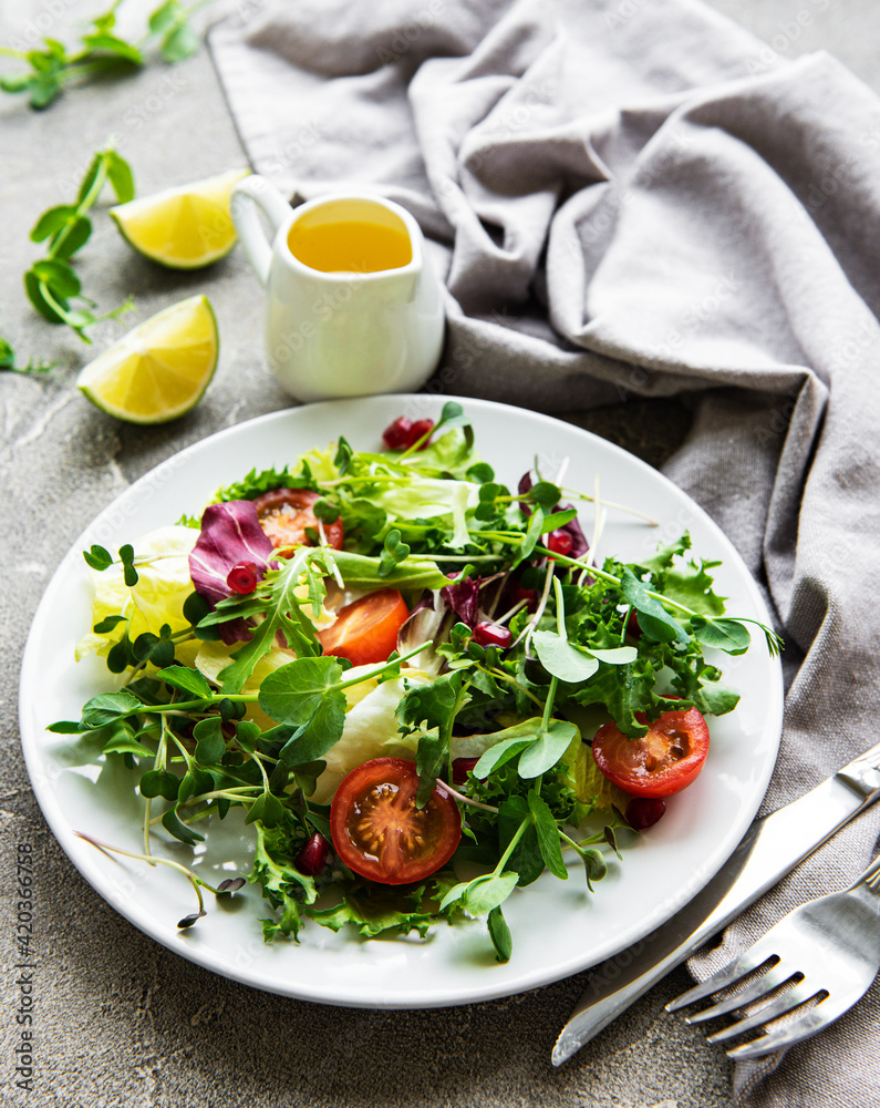 Fresh green mixed  salad bowl with tomatoes and microgreens  on  concrete background. Healthy food, top view.