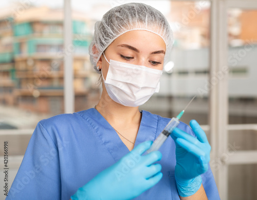 Portrait of lady doctor with vial and syringe in her hands in professional protective clothing - medical mask and surgical cap